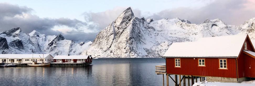 A fisherman's cabin covered in snow on top of the water with views over Reinefjorden and the mountain Olstind.